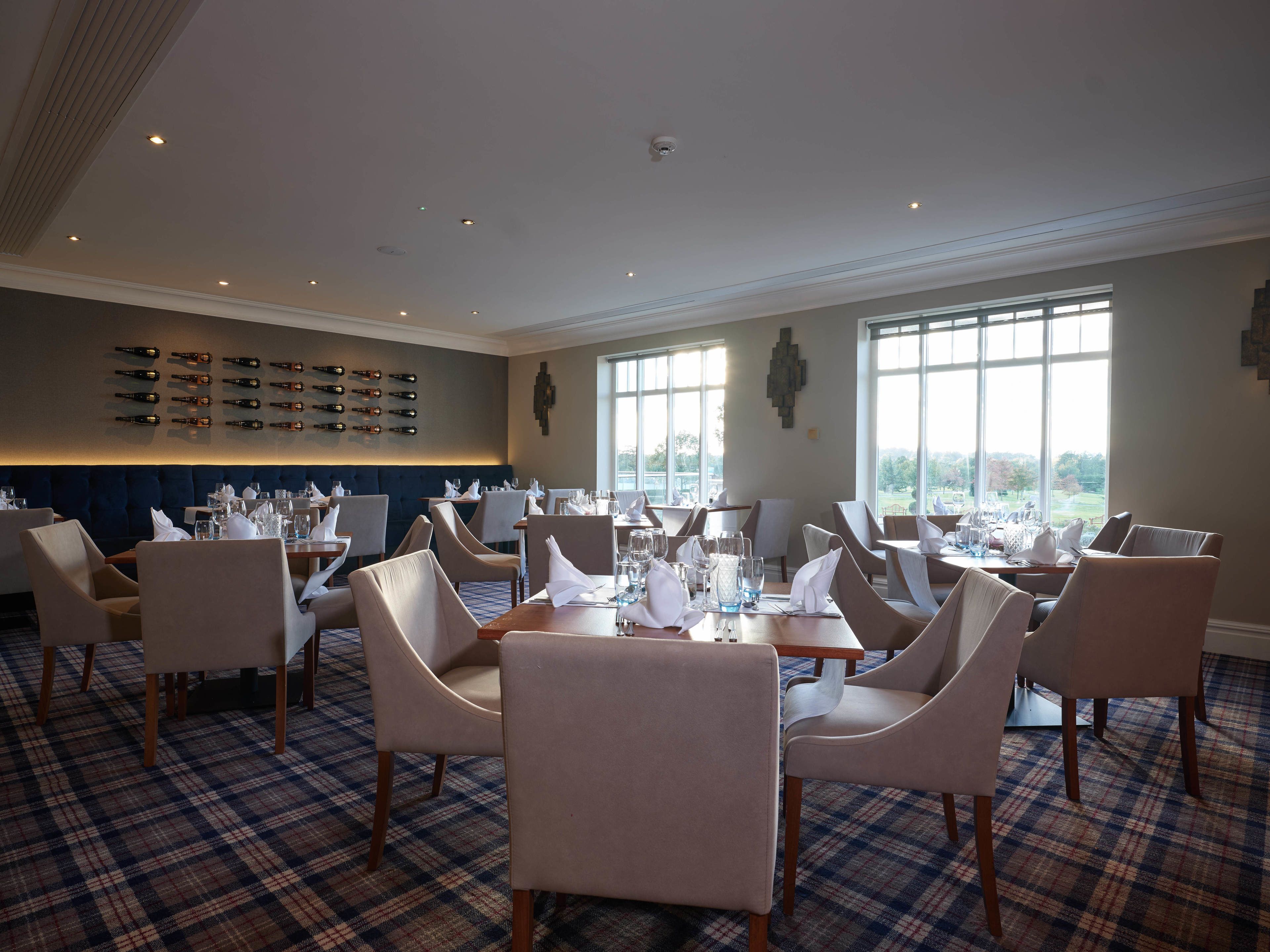 A restaurant with a checkered floor, multiple tables set with white napkins and glasses, and a wall of wine bottles.