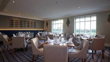 A restaurant with a checkered floor, multiple tables set with white napkins and glasses, and a wall of wine bottles.