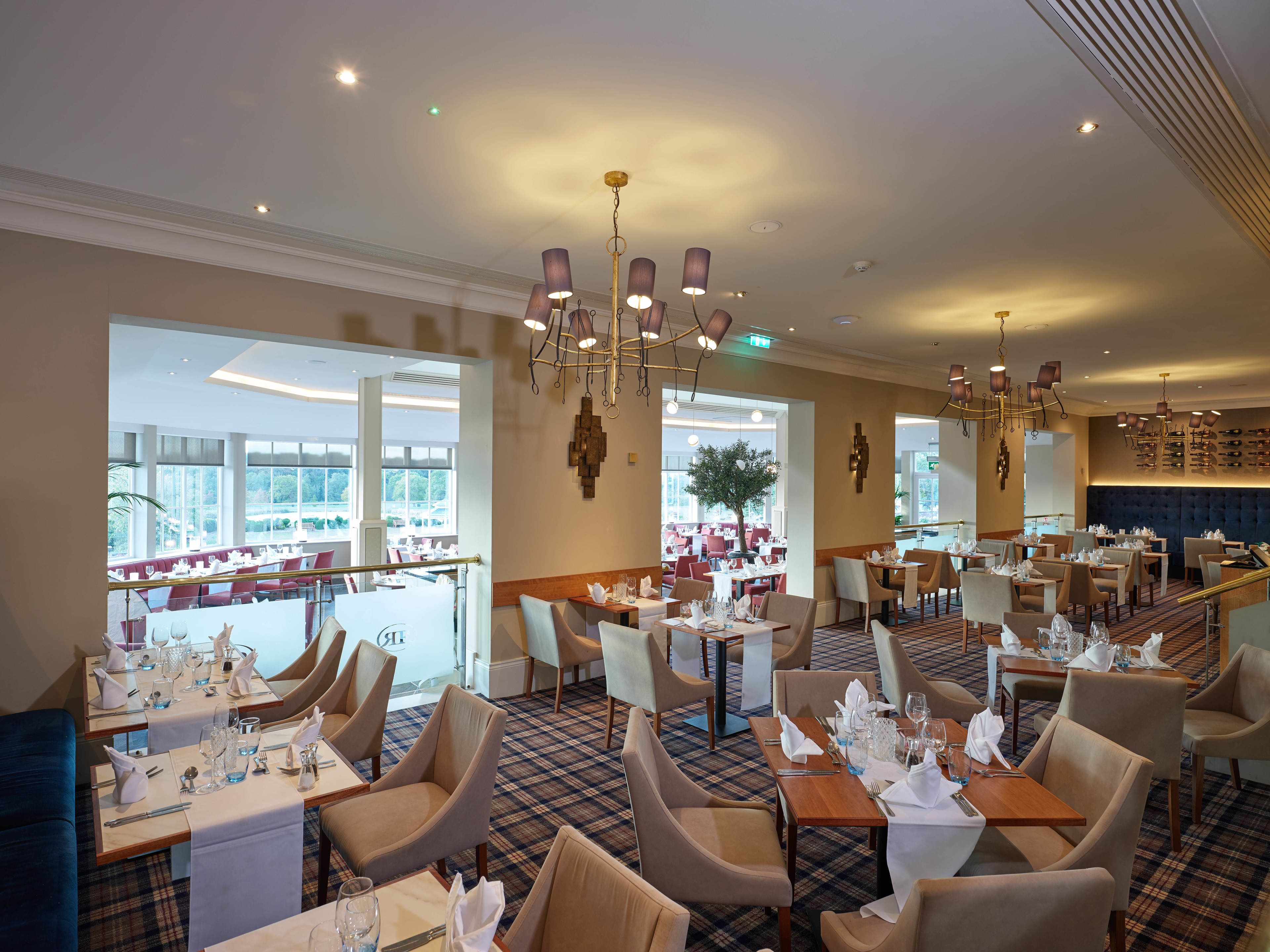 En rummelig restaurant med høje lofter, moderne lysekroner og forskellige siddepladser, herunder borde og båse.
