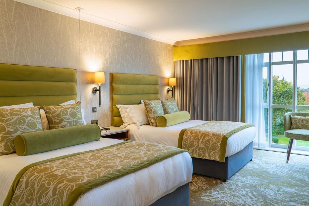 A hotel room with two beds, a large window, and a balcony.