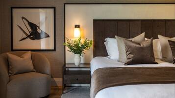 Ein modernes Hotelzimmer mit Bett, Nachttisch, Sessel, gerahmtem Kunstwerk und Wandlampe.