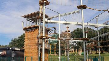 An outdoor adventure park with climbing walls, ropes, and a wooden climbing structure.