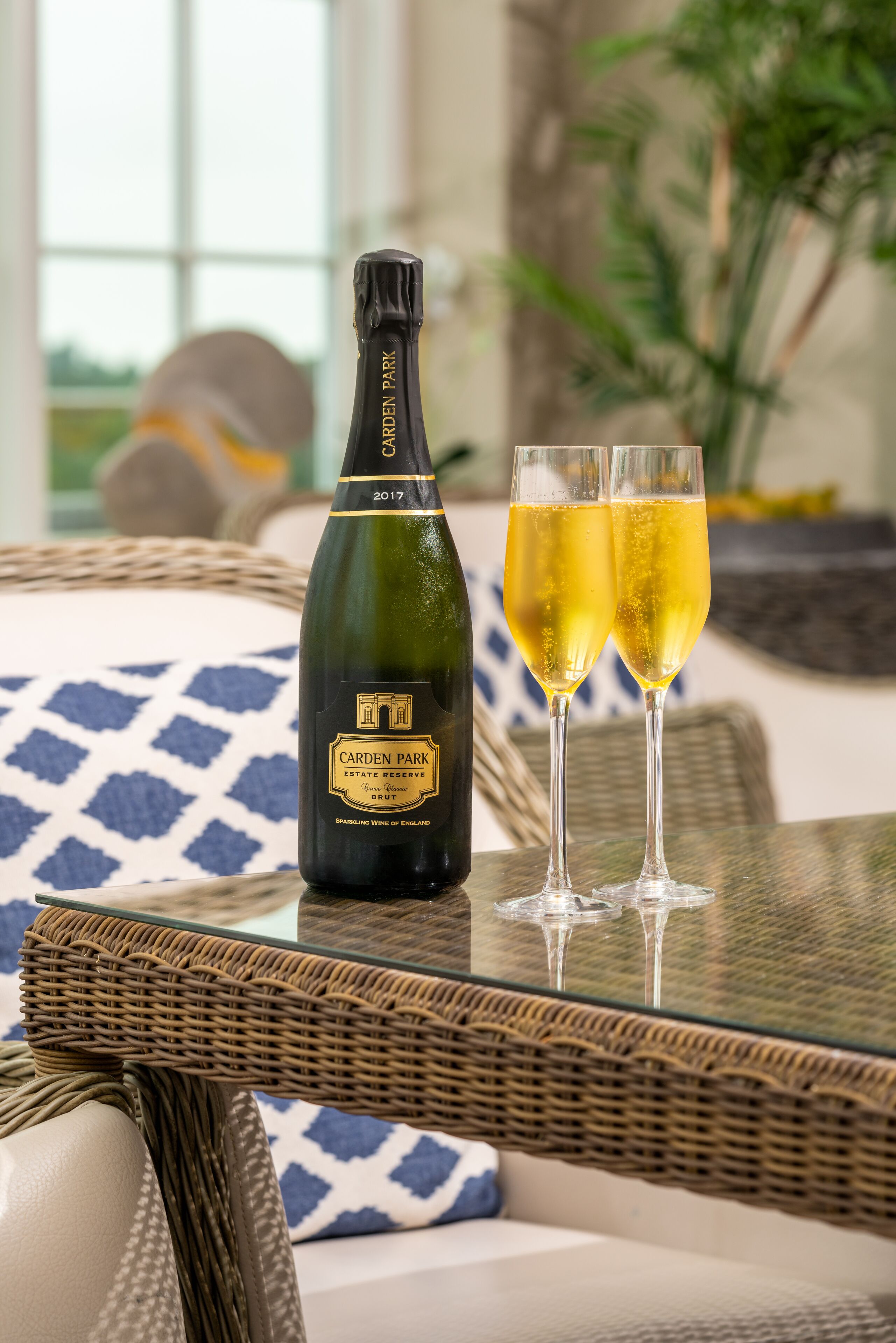 A bottle of Carden Park Estate Reserve sparkling wine and two glasses on a glass table.