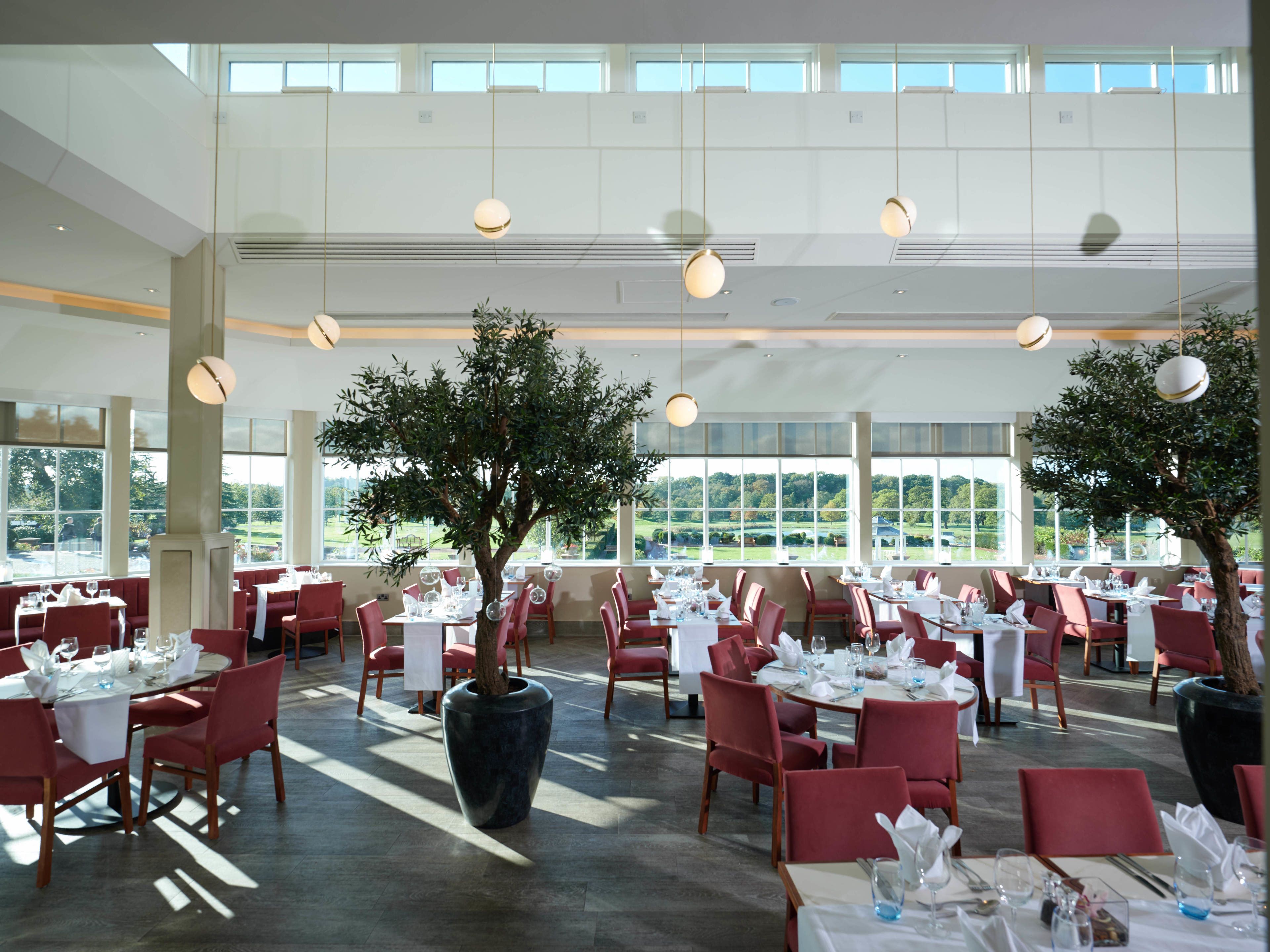 Un'ampia sala ristorante con numerosi tavoli e sedie, ampie finestre che offrono vista sull'esterno e lampadari a sospensione.