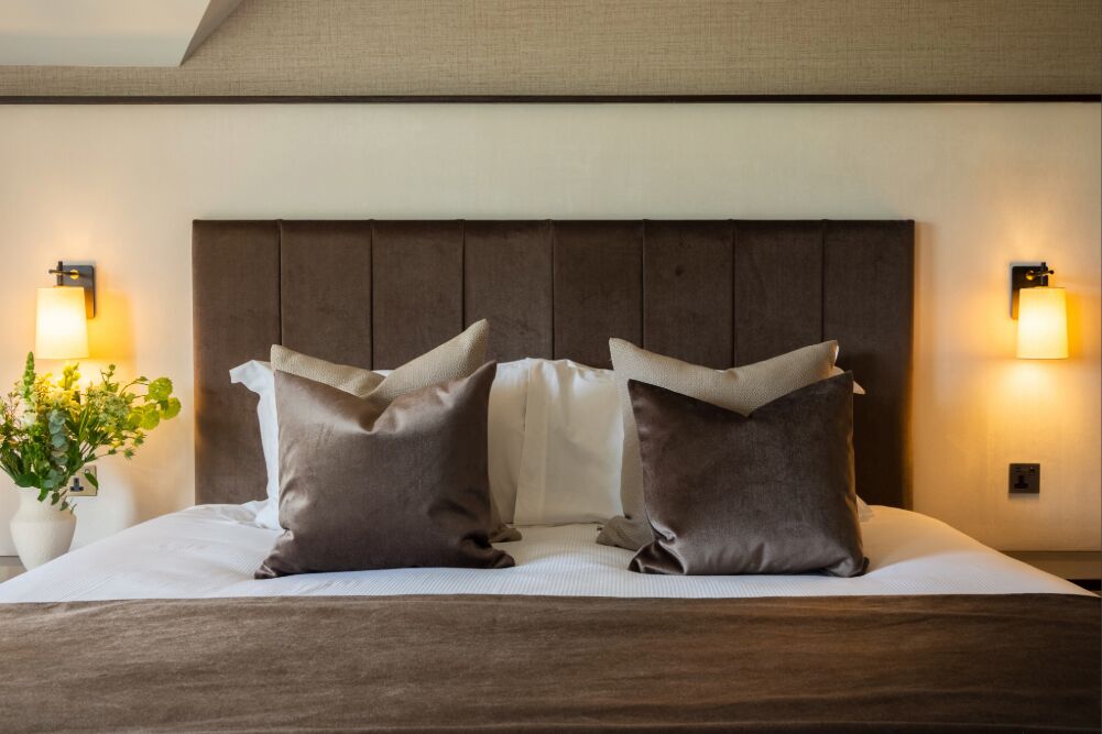 A neatly made bed with a wooden headboard, two pillows, and two wall-mounted lamps on either side.