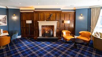 A room with a fireplace, plaid carpet, and leather chairs.