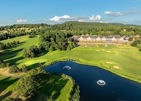 A golf course with a pond, a clubhouse, and surrounding greenery.