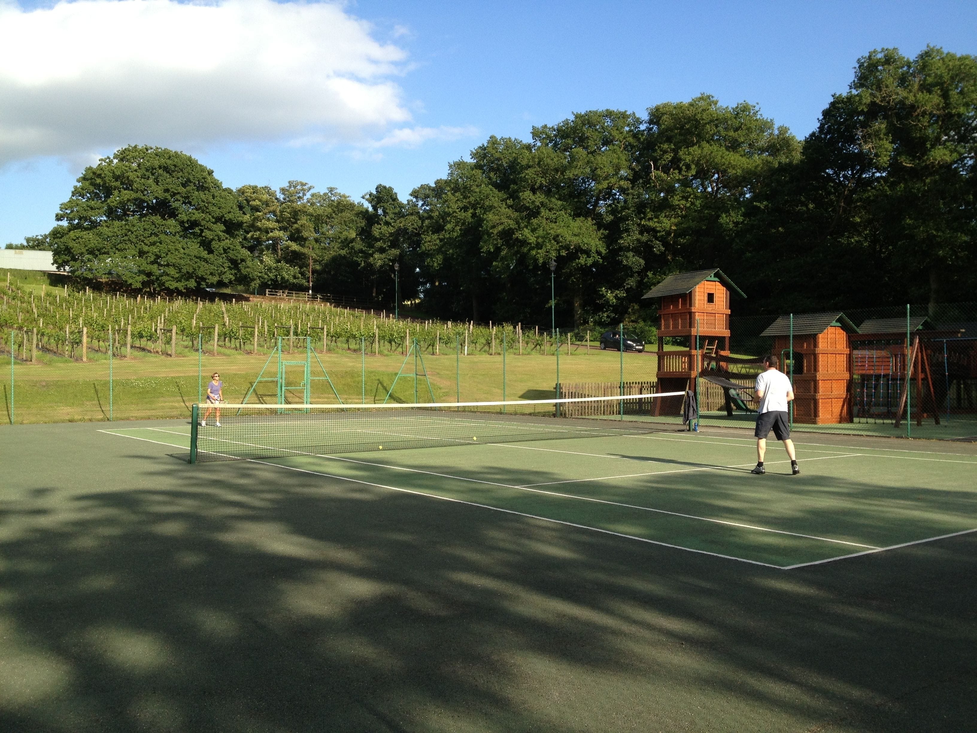 Una cancha de tenis con una red, rodeada de árboles y una estructura de madera.