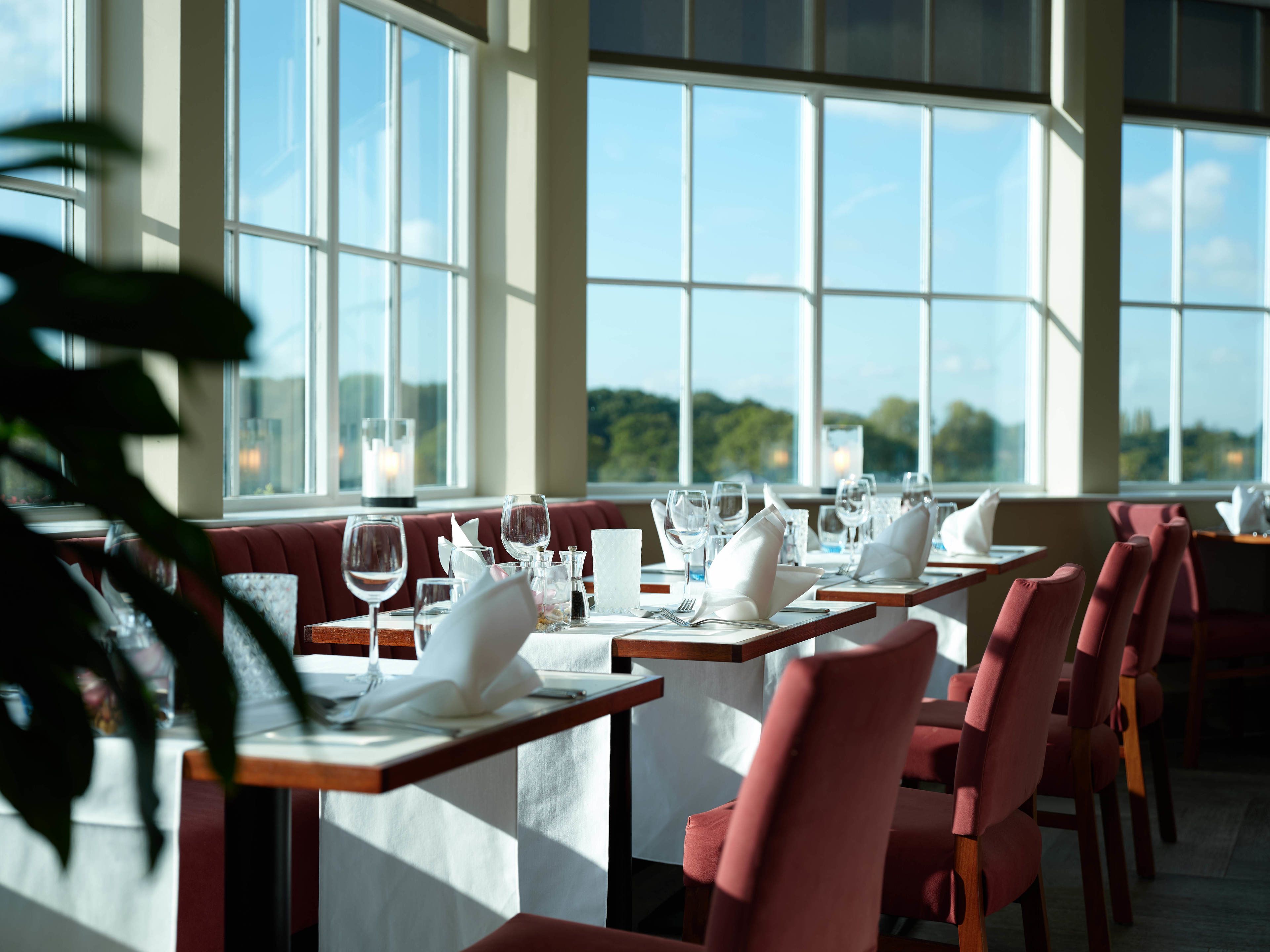 Un restaurante con mesas dispuestas para comer, ventanas amplias y vistas al exterior.