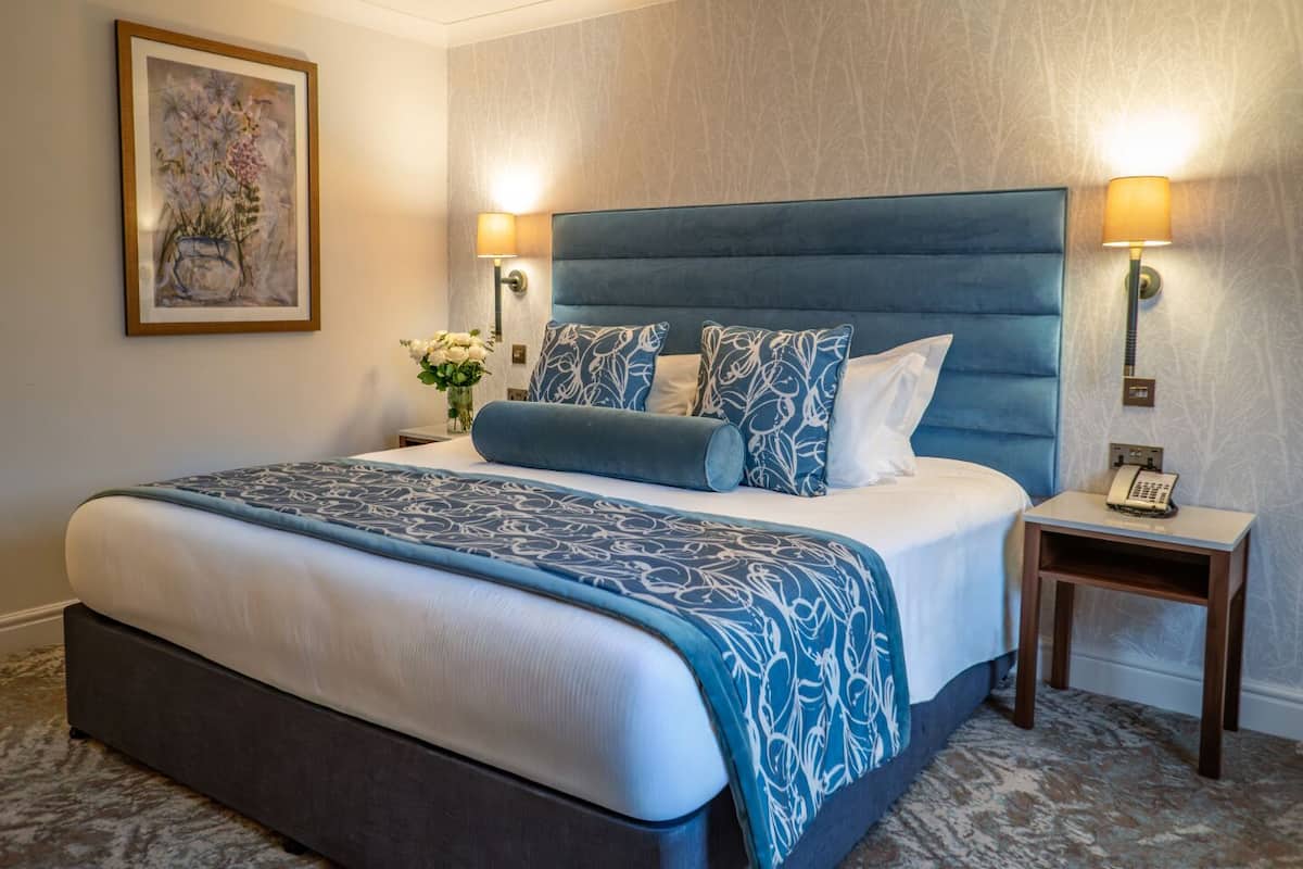 A hotel room with a large bed, two bedside lamps, a nightstand with a phone, and a framed picture on the wall.