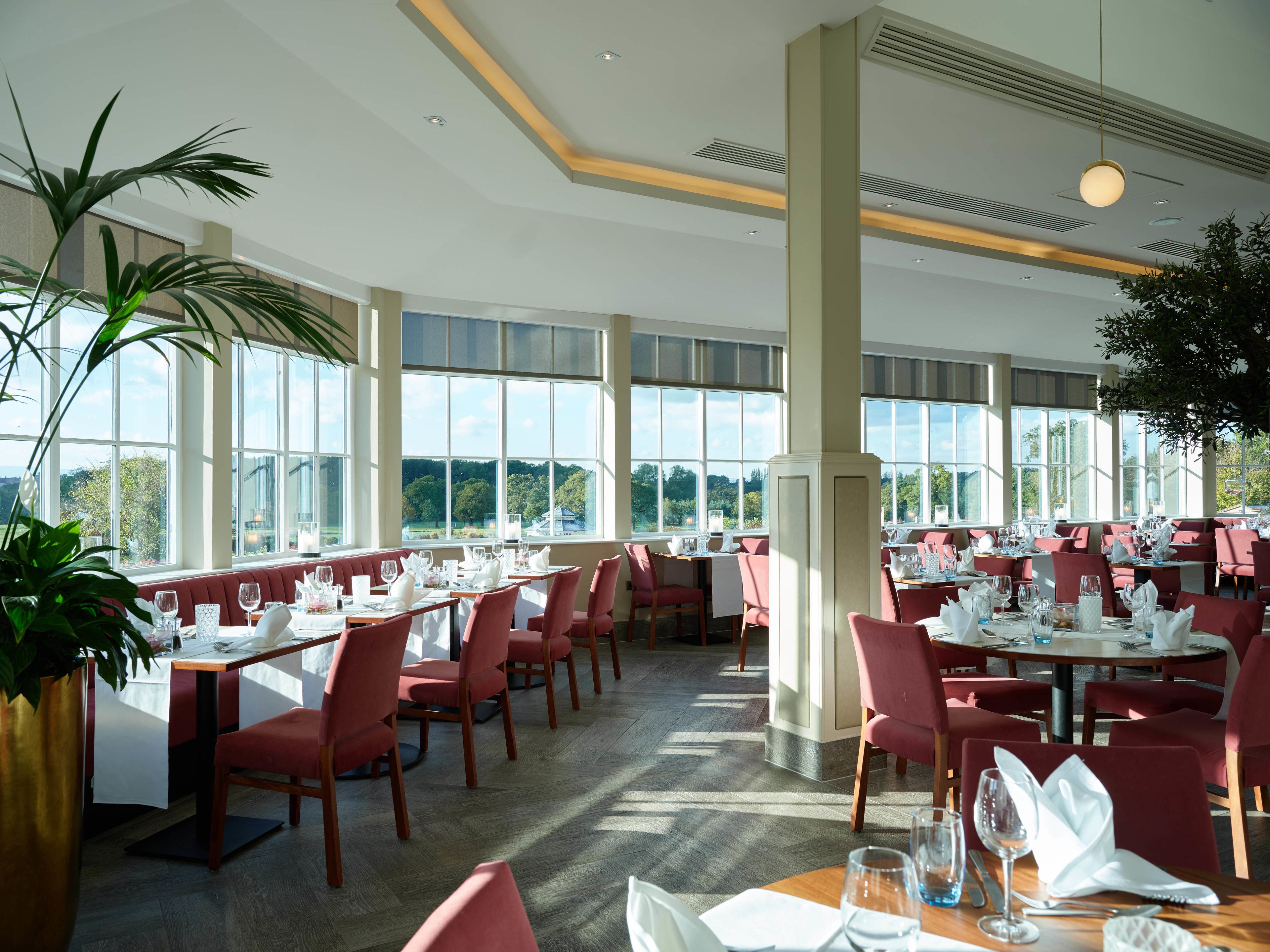 Un'ampia sala da pranzo con diversi tavoli e sedie, grandi finestre che offrono vista all'esterno e un design moderno del soffitto.