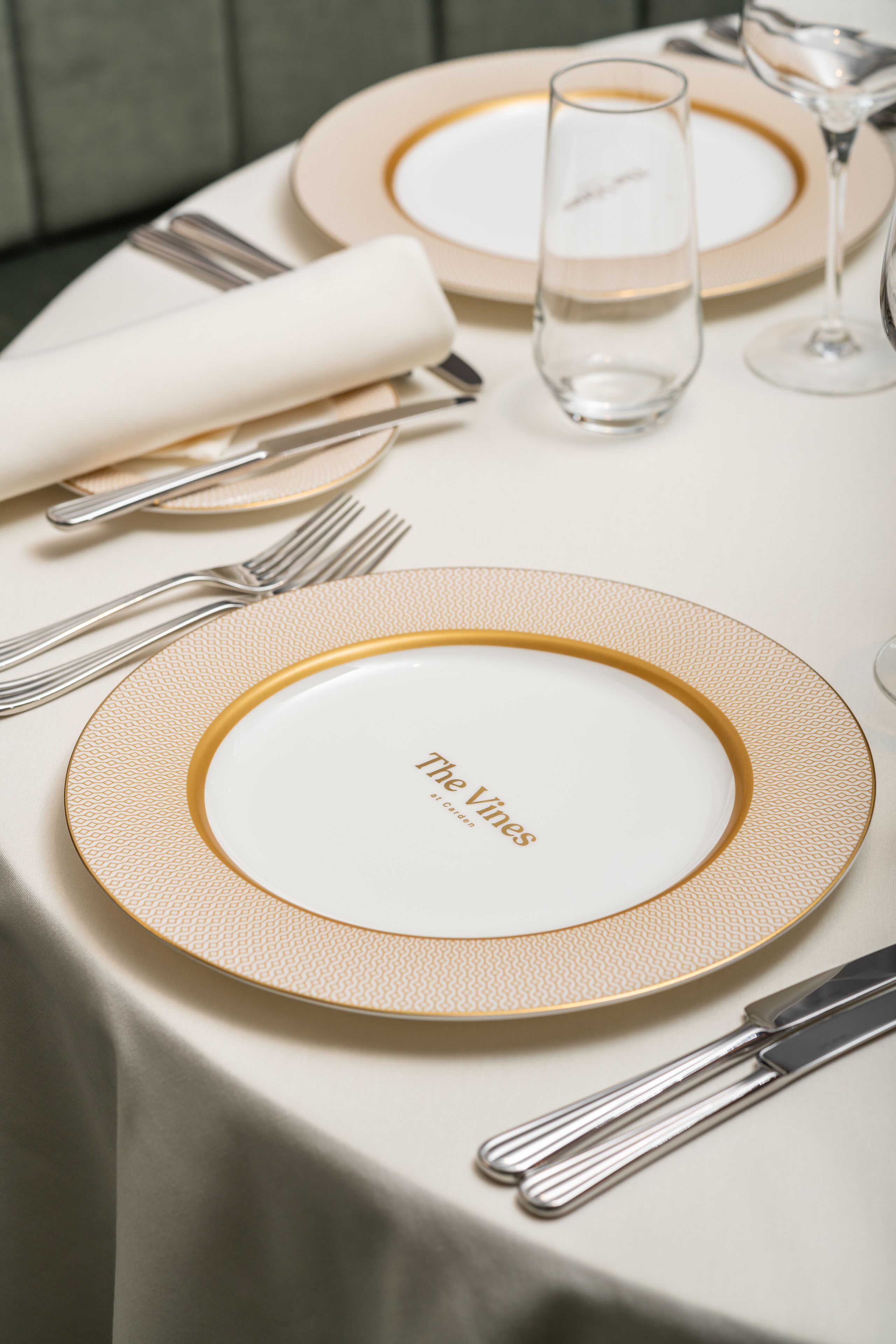 A table set with a gold rimmed plate, a folded white napkin, and silverware.