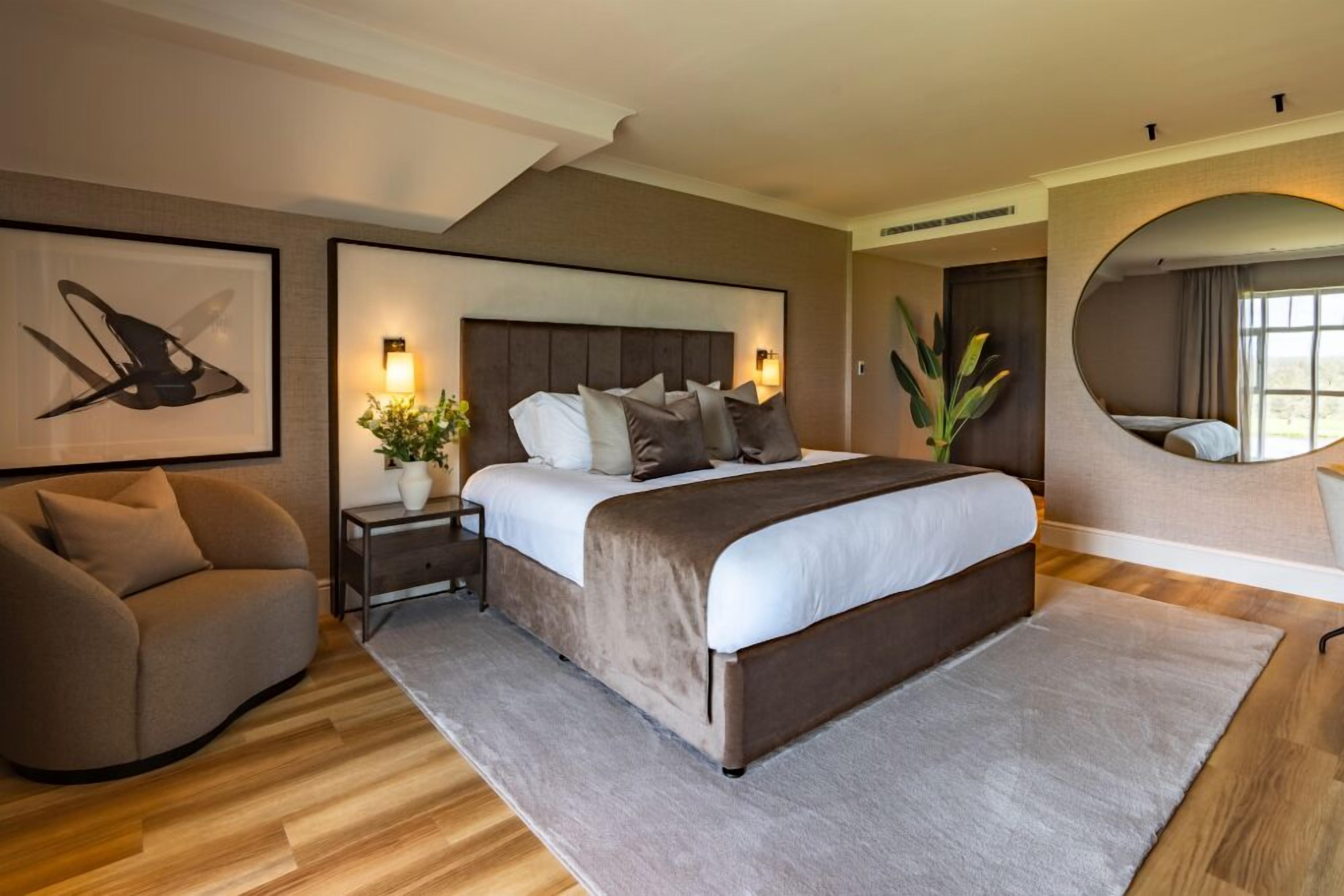 Un dormitorio moderno con una cama grande, un sofá, una mesita de noche con lámpara y un espejo.