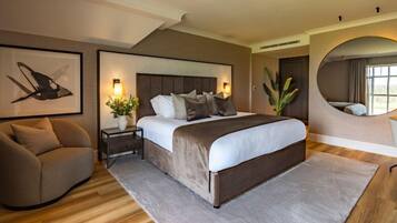 Un dormitorio moderno con una cama grande, un sofá, una mesita de noche con lámpara y un espejo.
