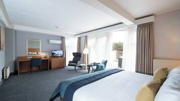 Ein Hotelzimmer mit einem großen Bett, einem Schreibtisch mit Computer, einem Sessel und einem kleinen Tisch.