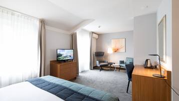 A hotel room with a bed, a television, a desk with a lamp, a chair, and a desk lamp.