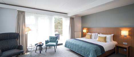 A hotel room with a large bed, a sofa, a small table, and a chair.