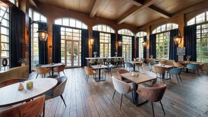A spacious dining area with multiple tables and chairs, large windows with curtains, and wooden flooring. - Bilderberg Résidence Groot Heideborgh (Garderen)