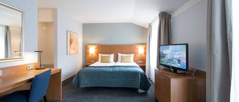 Habitación de hotel con cama, escritorio, silla, televisión y un amplio ventanal con cortinas.