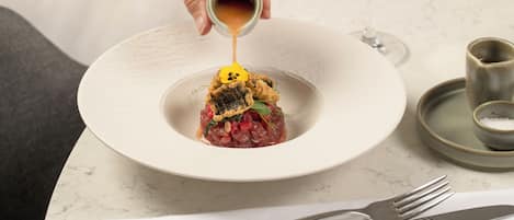A person pouring a sauce over a dish on a white plate.