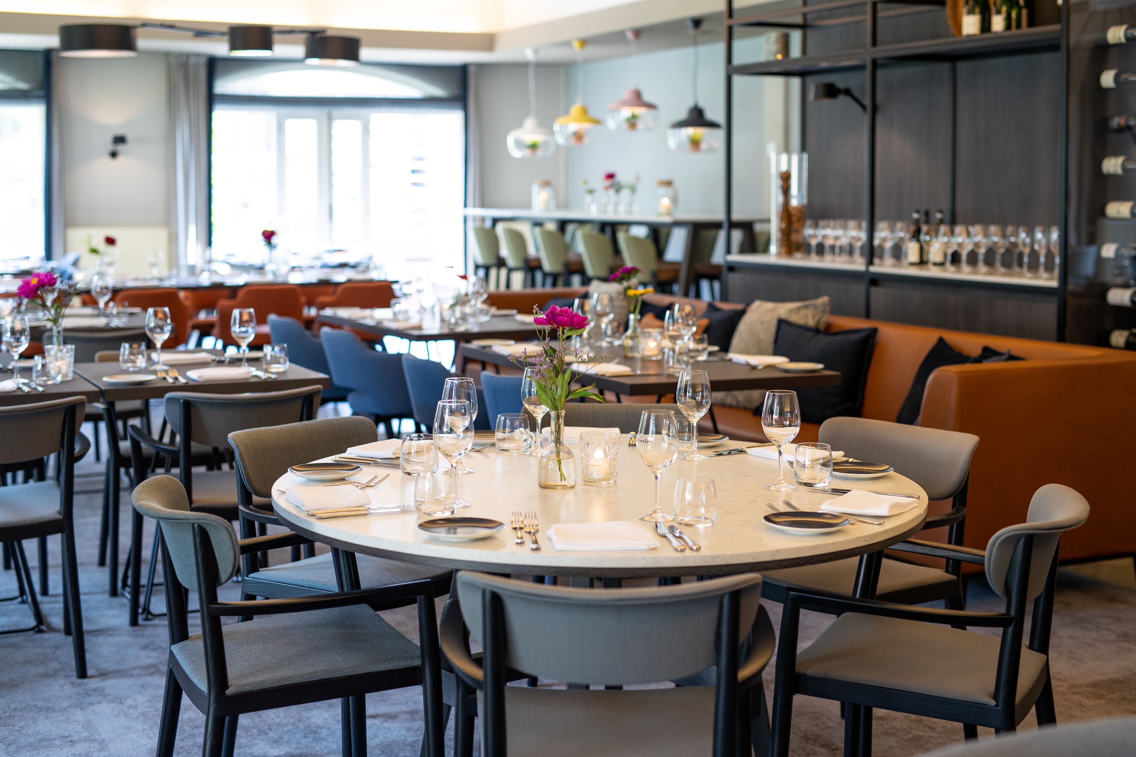 A restaurant with round tables set for dining, chairs, and a bar area with shelves of bottles.