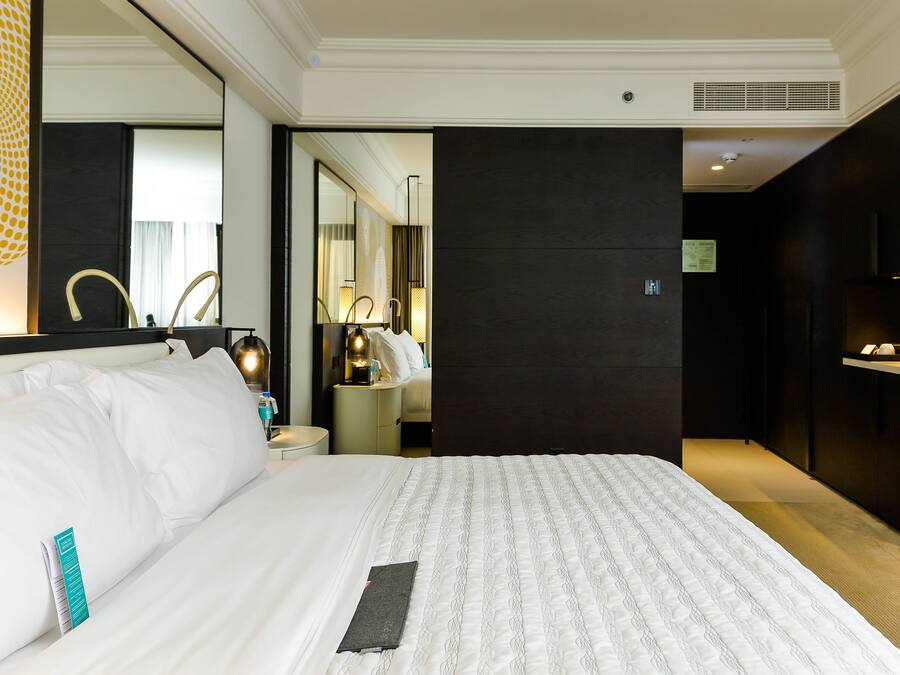 Une chambre d’hôtel avec un grand lit, une table de chevet avec une lampe, un miroir et un mur de couleur sombre.