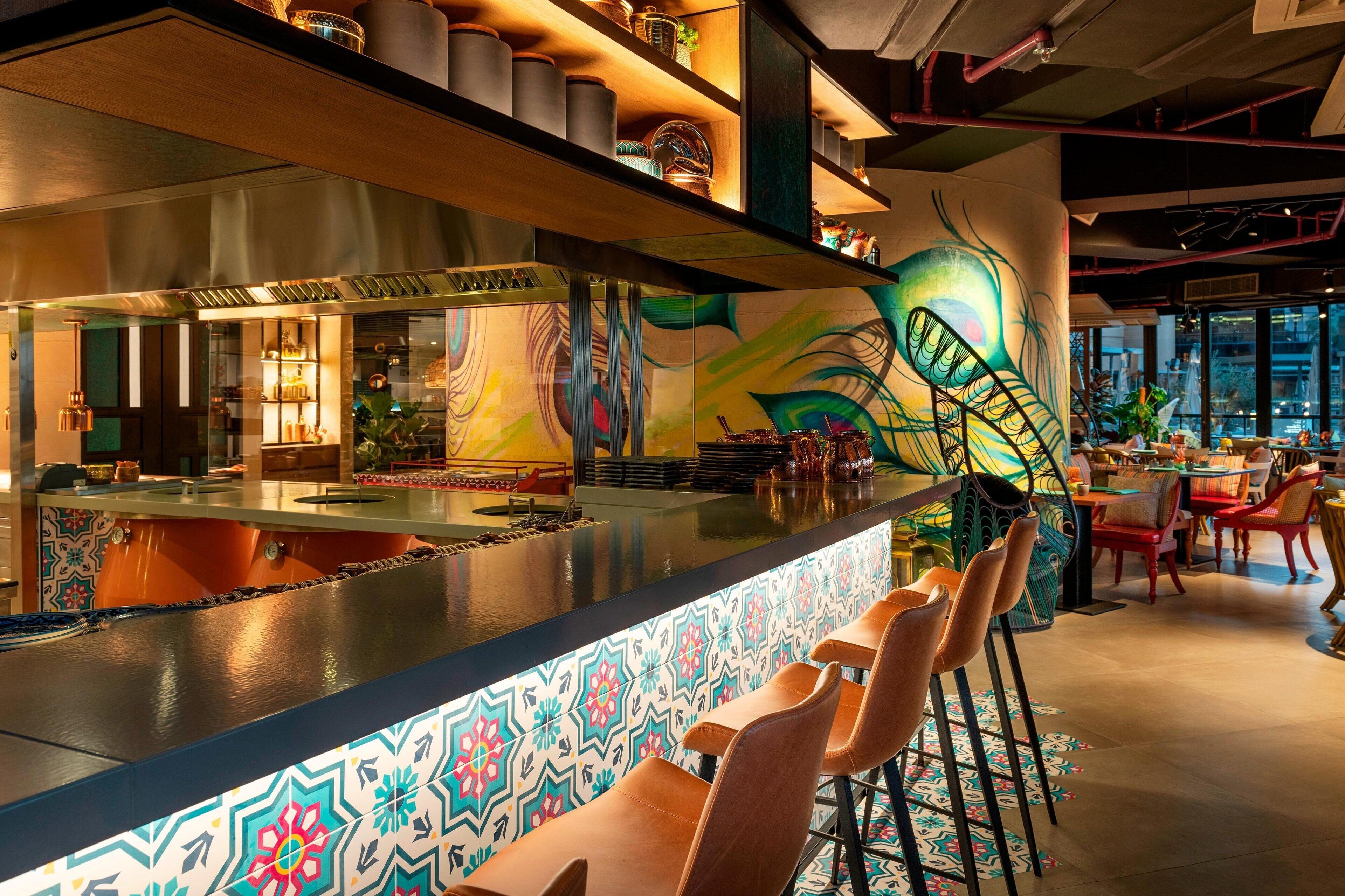 Una zona de bar con un revestimiento de azulejos de colores, taburetes y un mural en la pared.