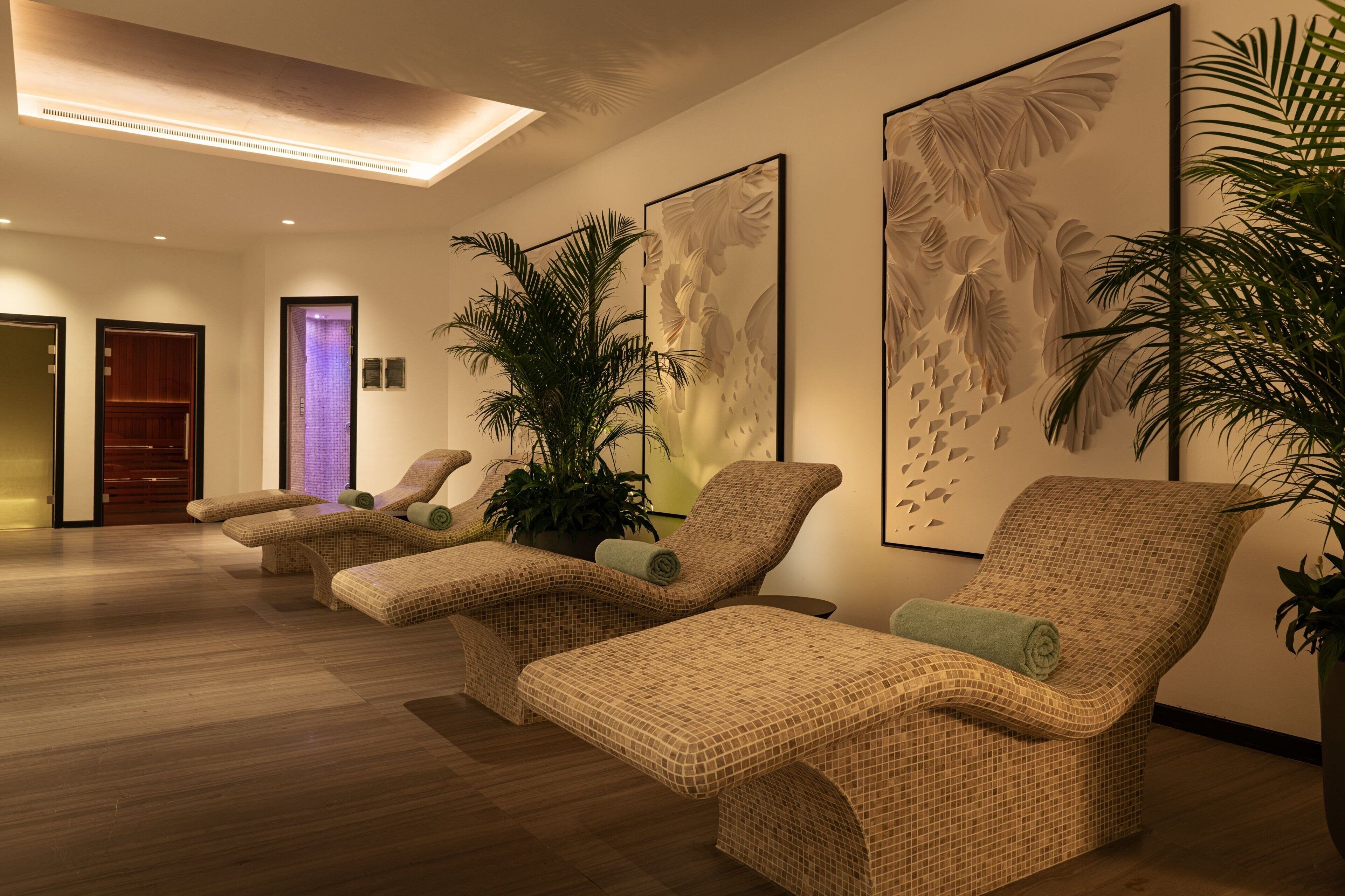 A spa area with three wicker lounge chairs, a large potted plant, and a wall with a leaf pattern.