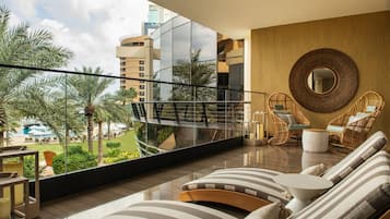 Uma sala de estar moderna com varanda, janelas amplas e vista para palmeiras e edifícios.