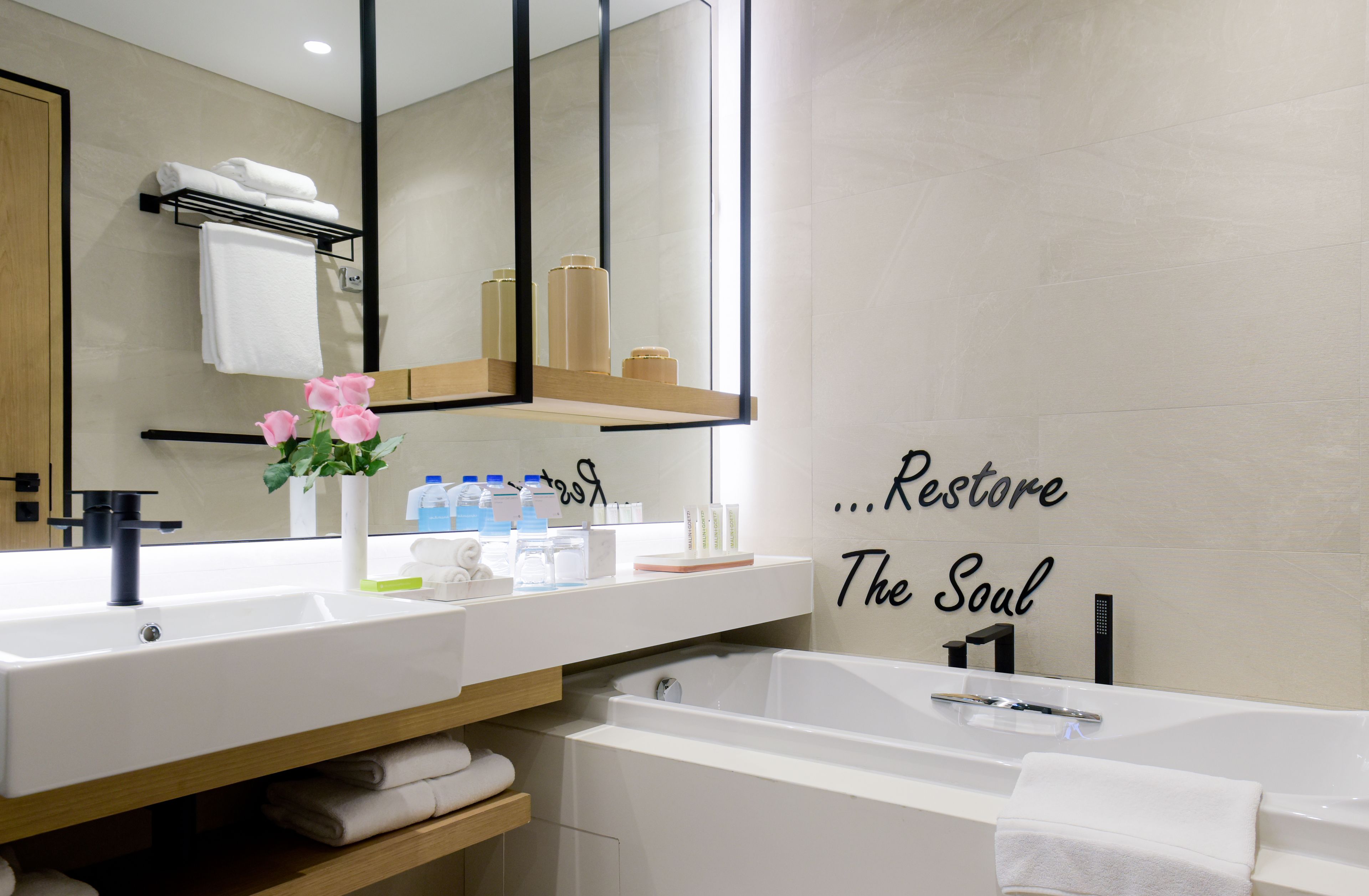 A modern bathroom with a large mirror, two sinks, a bathtub, and a towel rack.