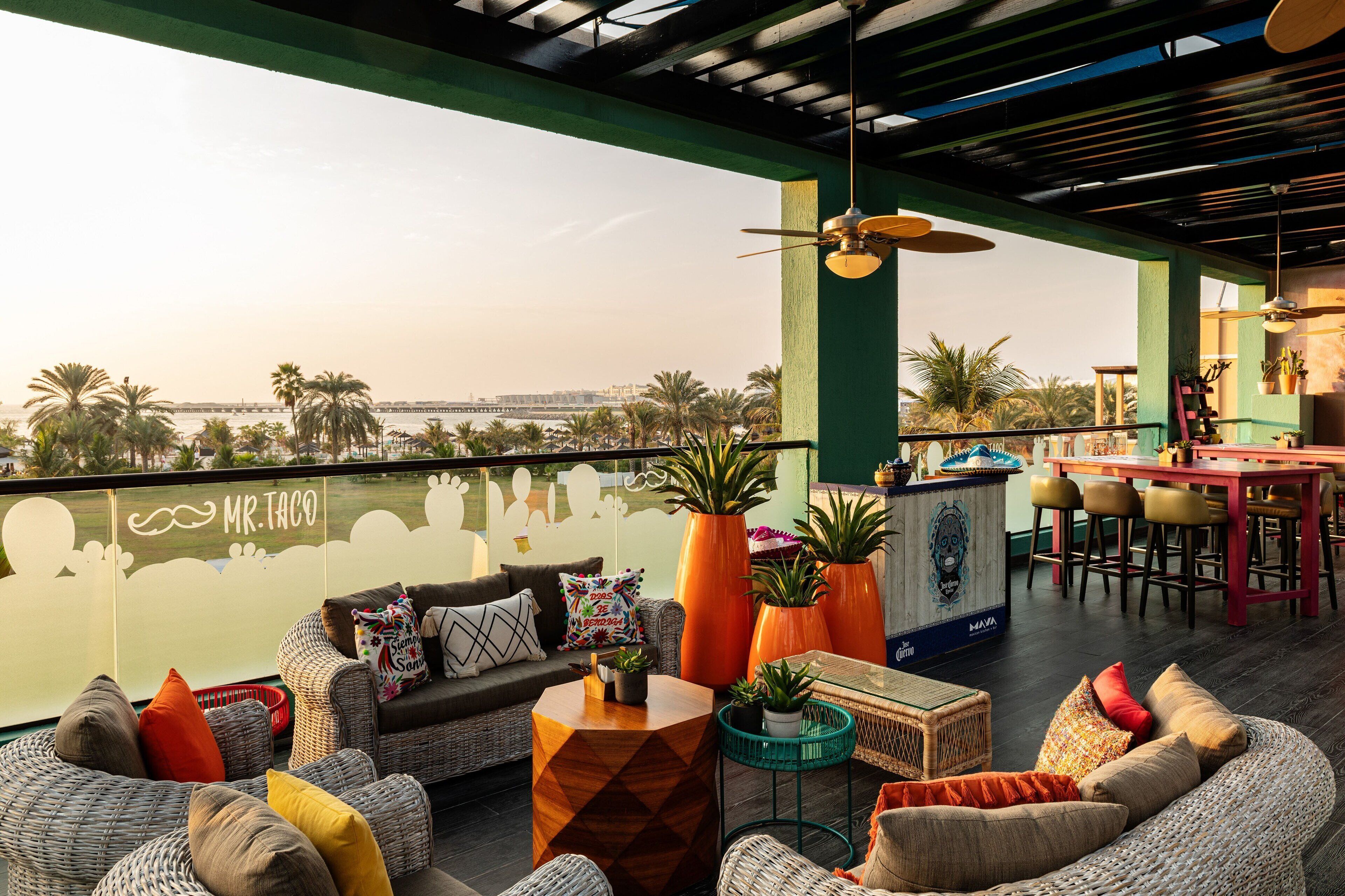 Un bar en la azotea con mobiliario de mimbre, plantas en macetas y vistas panorámicas de la ciudad.