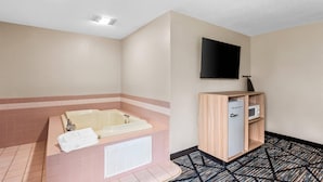 A bathroom with a bathtub, a toilet, a sink, a mirror, a television mounted on the wall, and a cabinet with a microwave.