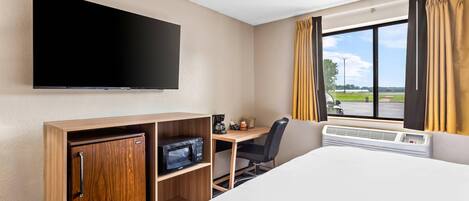 A hotel room with a bed, a desk with a chair, a flat-screen TV, a microwave, and a window with curtains.
