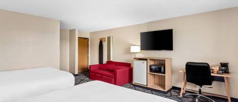 A hotel room with two beds, a red sofa, a desk with a computer, a TV, and a refrigerator.