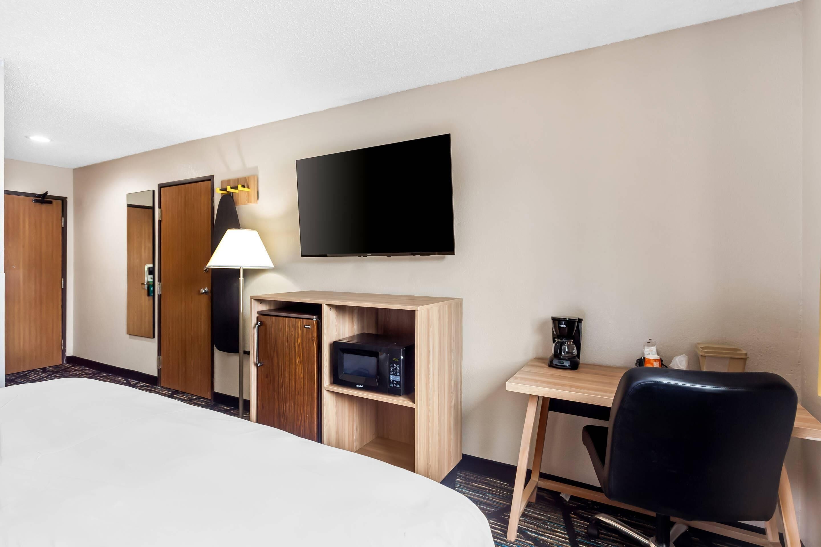 A hotel room with a bed, a desk with a chair, a television, a microwave, and a coffee maker.