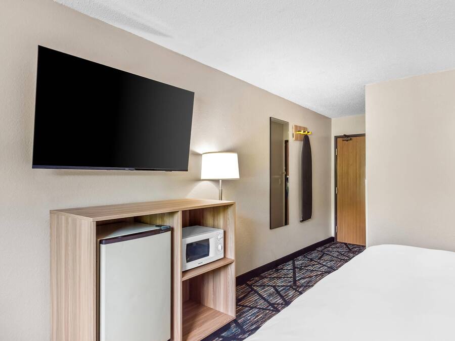 A hotel room with a bed, a flat-screen TV mounted on the wall, a microwave, a lamp, and a door.