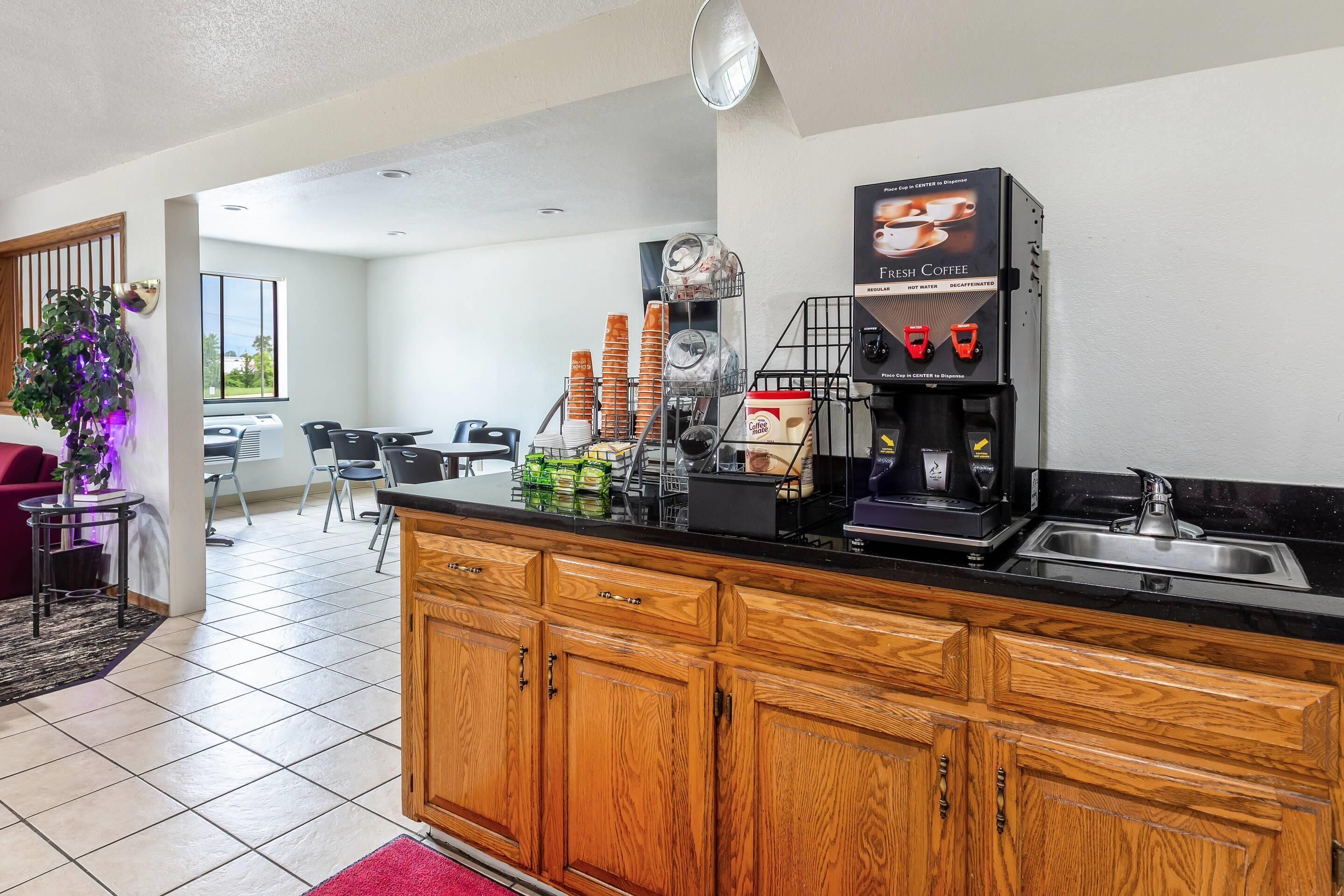 A modern kitchen with a coffee machine, a sink, and a dining area with chairs and a table.