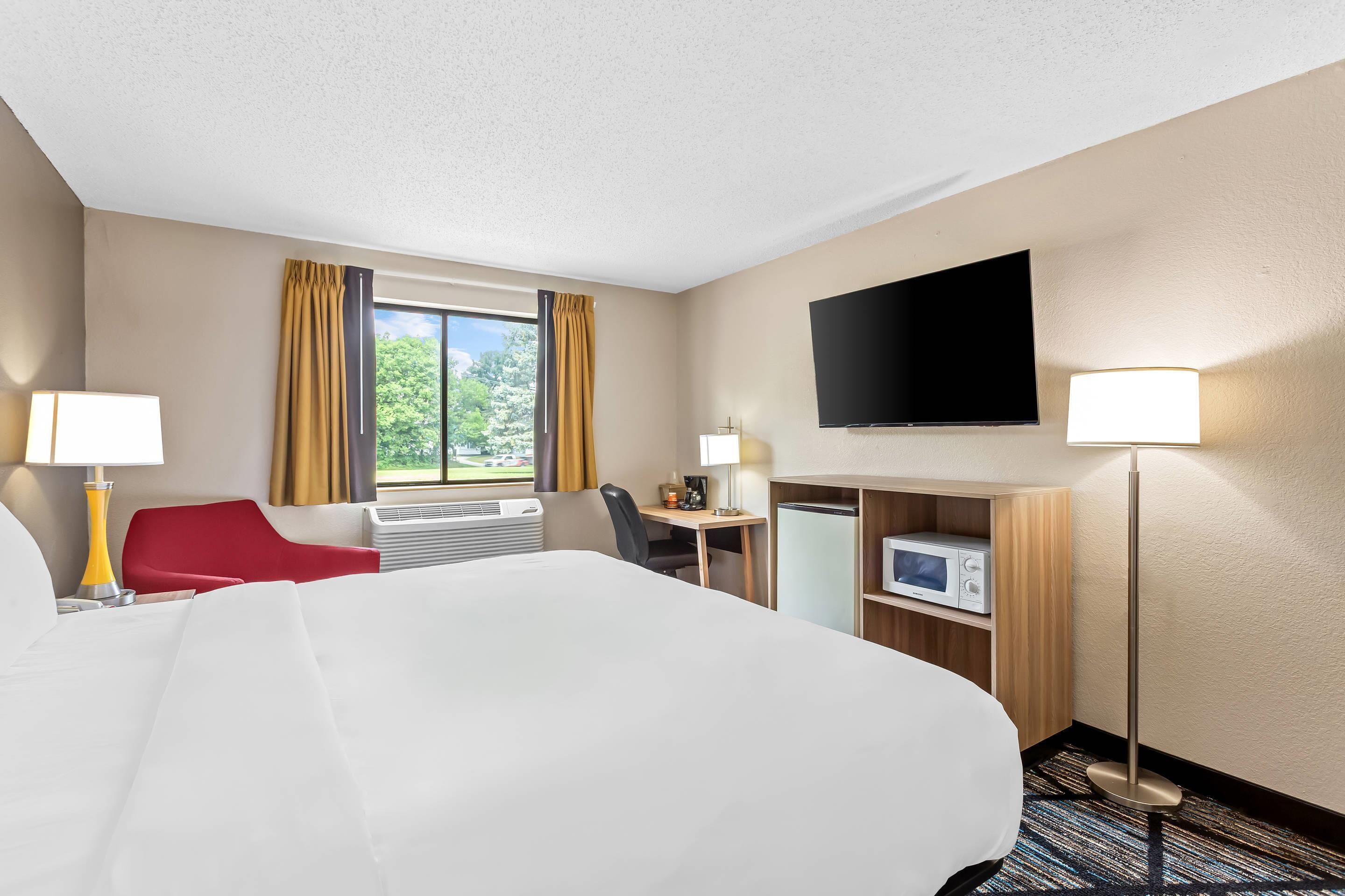 A hotel room with a large bed, a desk, a chair, a TV, and a microwave.