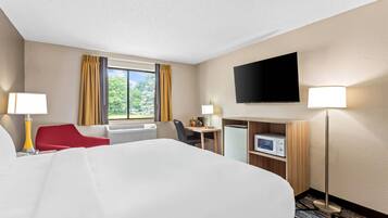 A hotel room with a large bed, a desk, a chair, a TV, and a microwave.