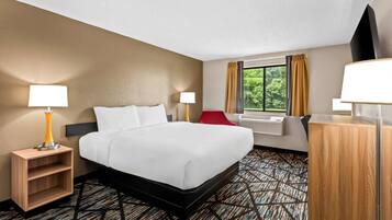 A hotel room with a bed, two bedside lamps, a red chair, a desk, and a window with curtains.