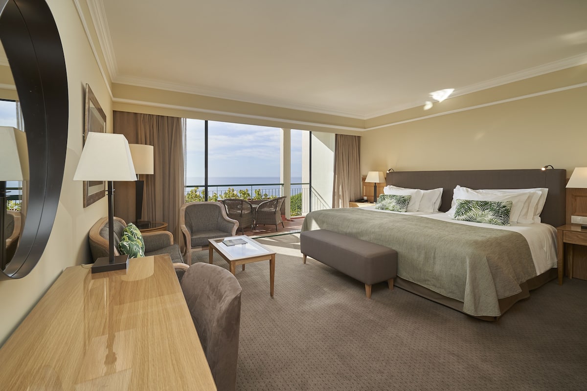 Habitación de hotel con una cama grande, un escritorio, una silla y vista al mar.
