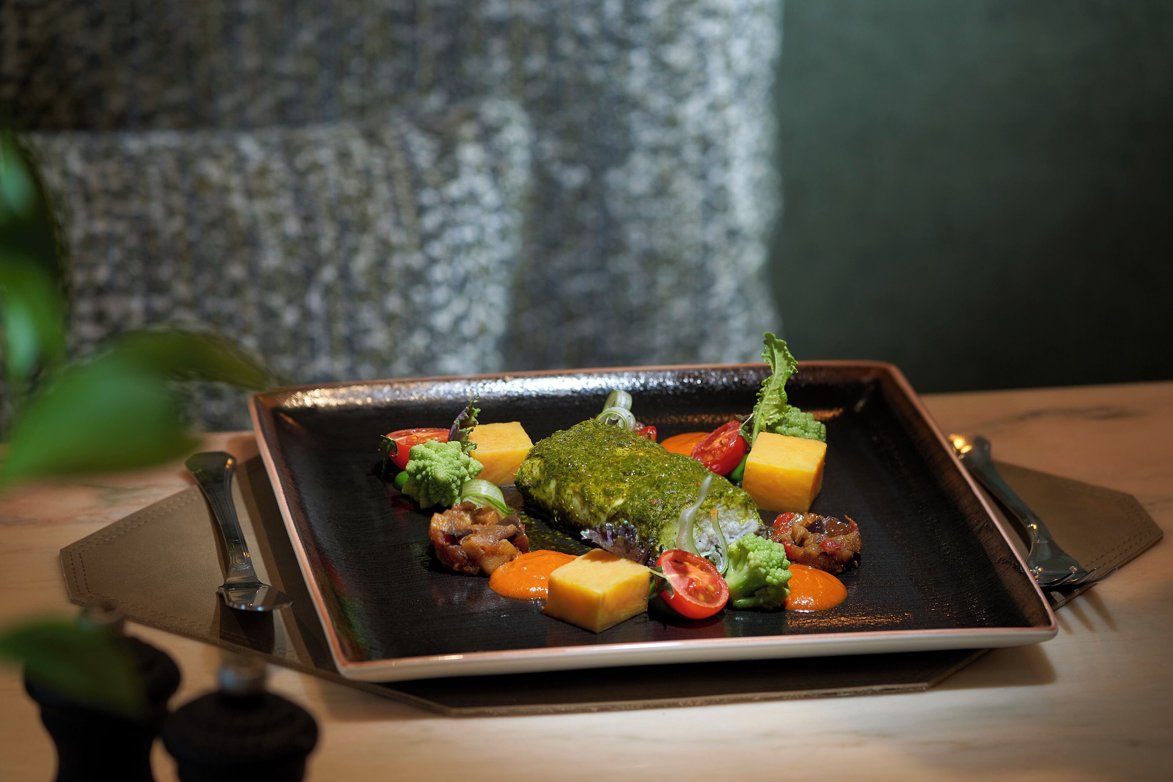 Un plato cuadrado con diversos alimentos, incluyendo un trozo de carne, verduras y un cubo de queso.