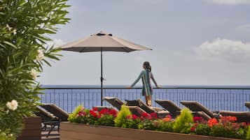 Un balcon avec des fauteuils de jardin, un grand parasol et une vue sur la mer.
