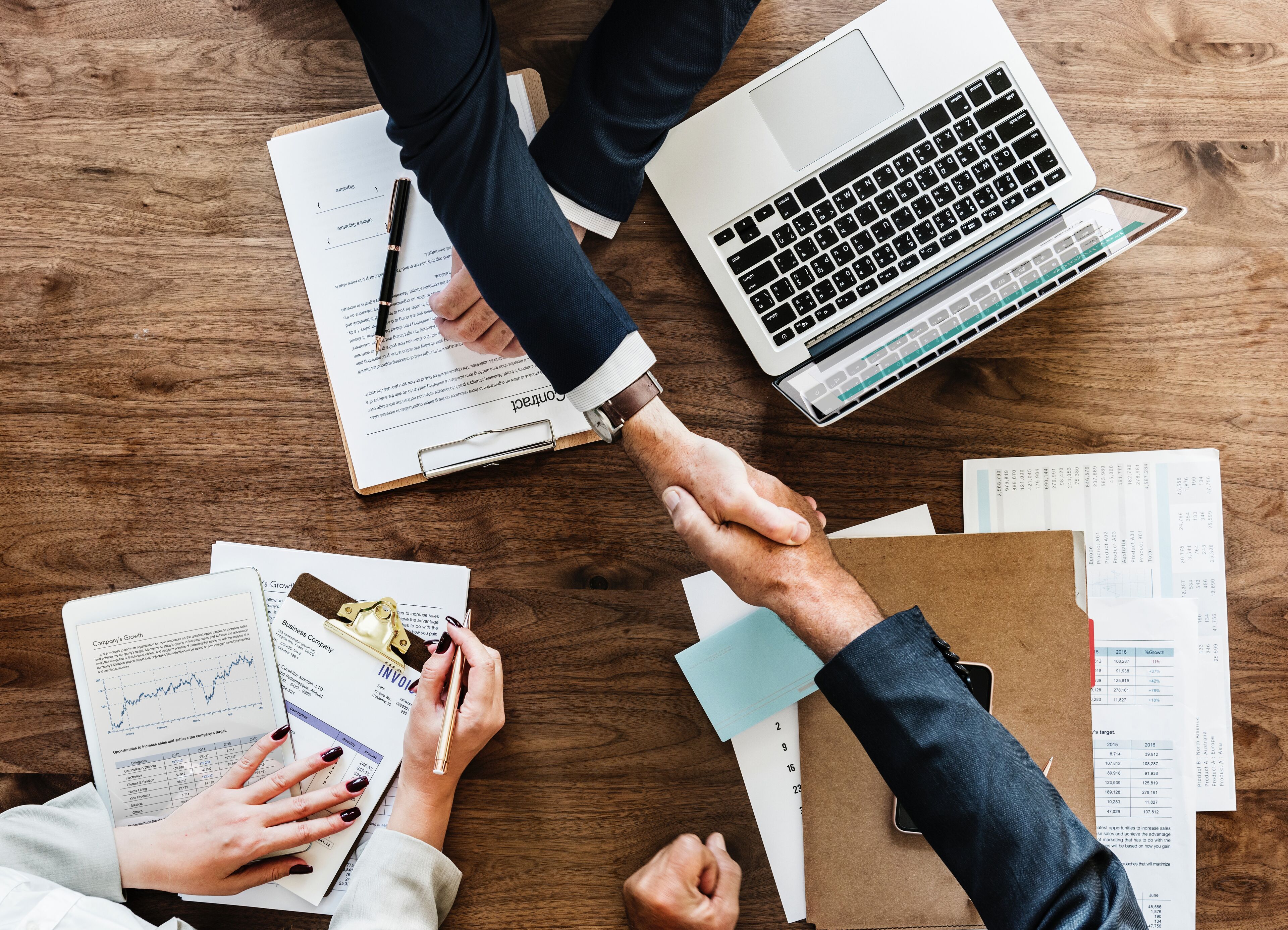 Una reunión de negocios con documentos, portátiles y un apretón de manos.