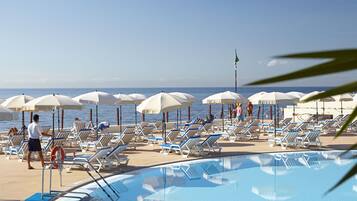 Un espace piscine équipé de chaises longues et de parasols, d’une bouée de sauvetage, et offrant une vue sur l’océan.