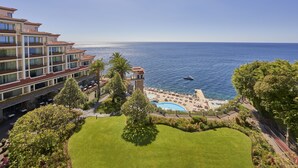 A hotel with a pool, lounge chairs, and a view of the sea. - The Cliff Bay, by PortoBay (Funchal)