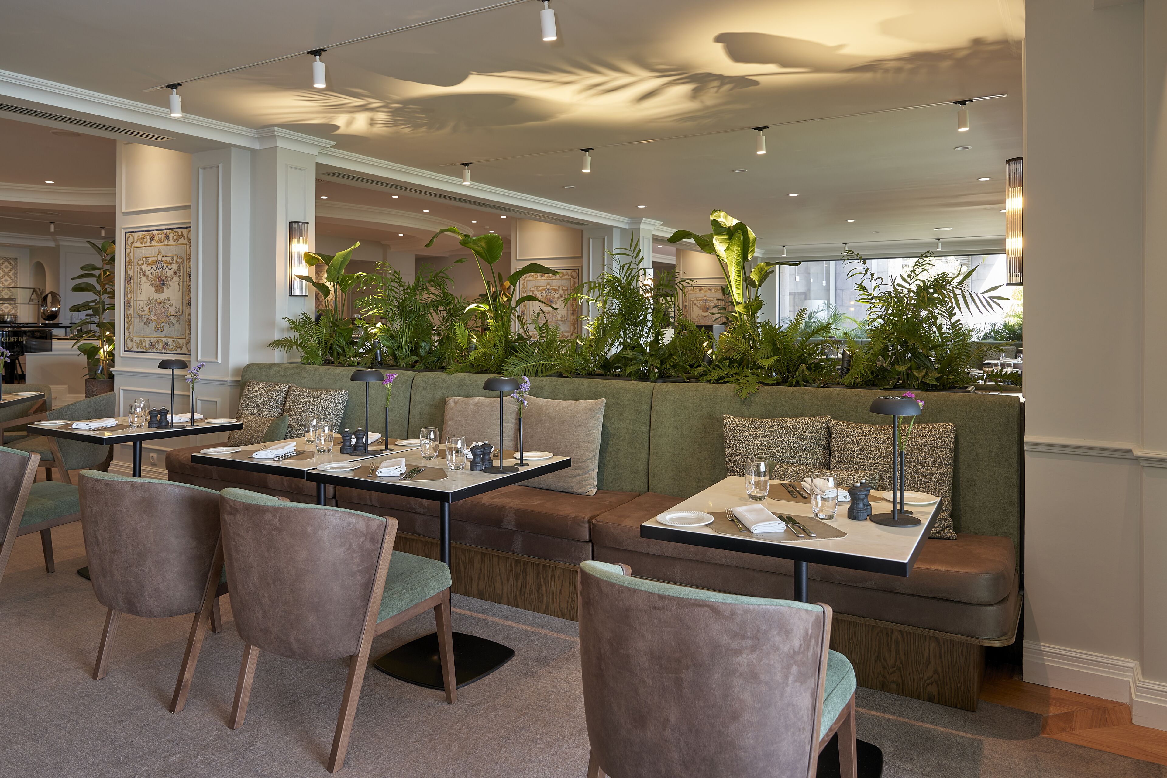 A modern dining area with green upholstered seating, wooden chairs, and tables set for dining.