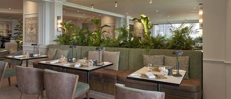 A modern dining area with green upholstered seating, wooden chairs, and tables set for dining.