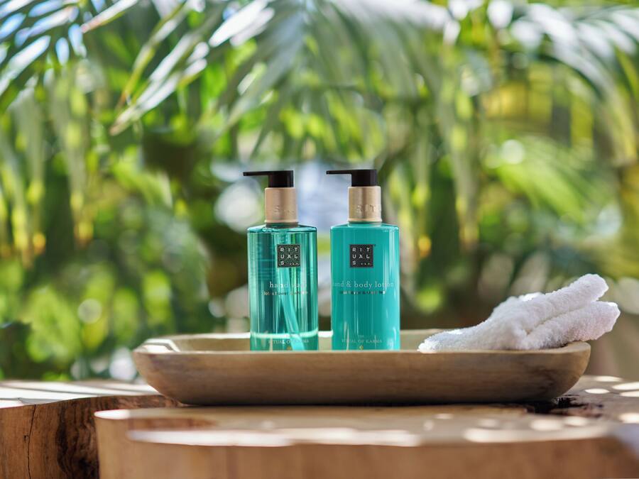 Une table en bois sur laquelle sont posées deux bouteilles de lotion pour les mains et le corps, ainsi qu’un bol contenant une serviette blanche.