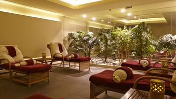 Un área de spa con sillones de mimbre, cojines rojos y un amplio arreglo de plantas de interior.